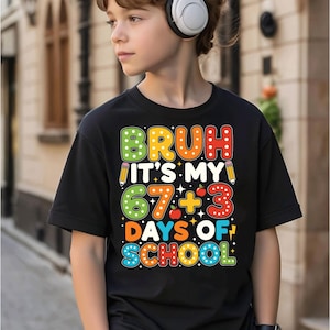 Peut inclure: T-shirt noir avec l'inscription colorée "BRUH IT'S MY 67 + 3 DAYS OF SCHOOL". Le texte est multicolore, avec des lettres vertes, oranges, rouges et bleues. Le t-shirt a un col rond et des manches courtes.