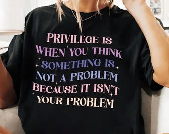 May include: Black t-shirt with the text "PRIVILEGE IS WHEN YOU THINK SOMETHING IS NOT A PROBLEM BECAUSE IT ISN'T YOUR PROBLEM" in pink, purple, and blue lettering.