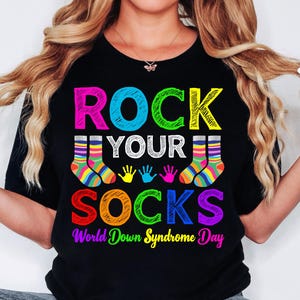 May include: Black t-shirt with the text "Rock Your Socks" in colorful letters. The text is surrounded by colorful handprints and socks. The bottom of the shirt reads "World Down Syndrome Day".