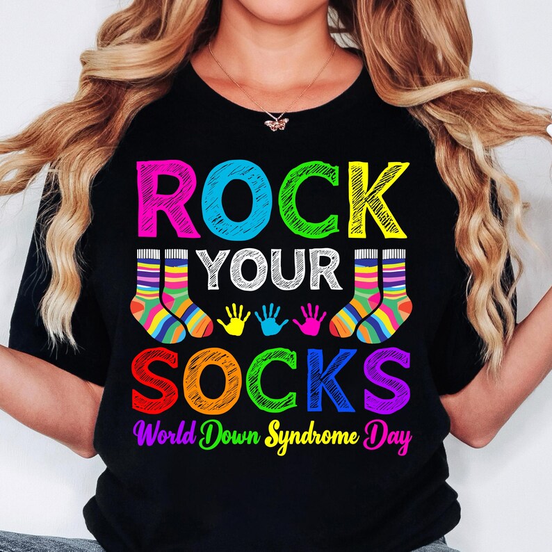 May include: Black t-shirt with the text "Rock Your Socks" in colorful letters. The text is surrounded by colorful handprints and socks. The bottom of the shirt reads "World Down Syndrome Day".