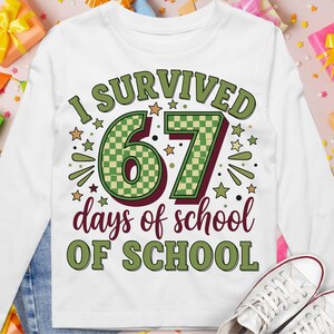 Peut inclure: T-shirt blanc à manches longues avec l'inscription "I SURVIVED 67 days of school OF SCHOOL" en vert, bordeaux et or. Le chiffre 67 est vert avec un motif à carreaux. Le t-shirt a un col rond et est en matière souple.