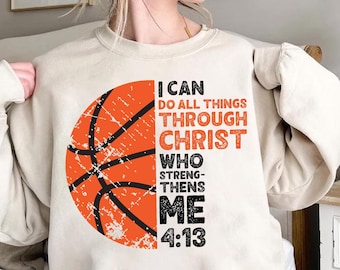May include: A beige sweatshirt featuring a distressed orange basketball graphic and the text "I CAN DO ALL THINGS THROUGH CHRIST WHO STRENGTHENS ME 4:13" in black and orange. The design is centered on the front of the long-sleeved top.