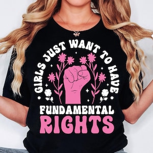 Peut inclure: T-shirt noir avec un graphique rose qui dit "Girls Just Want To Have Fundamental Rights" avec un poing levé et des fleurs.