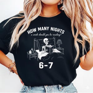 Op de afbeelding: Zwart sweatshirt met een witte afbeelding van een skelet dat in bed leest. De tekst erboven luidt "HOW MANY NIGHTS a week should you be reading?" en daaronder "6-7".