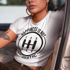 May include: White crew neck t-shirt with a black graphic of a gear shift and the text "HAPPINESS IS NOT AUTOMATIC". The shirt is short-sleeved.