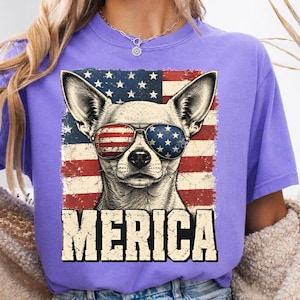 Peut inclure: Un t-shirt violet avec un motif représentant un chihuahua portant des lunettes de soleil aux motifs du drapeau américain. Derrière le chien se trouve un drapeau américain vieilli. Le texte MERICA est imprimé en grandes lettres capitales.