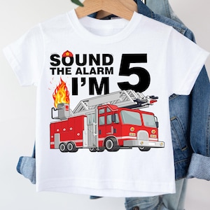 May include: White t-shirt with a red fire engine graphic and the text "Sound the alarm I'm 5".