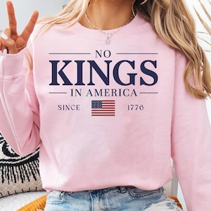 Peut inclure: Sweat-shirt rose avec le texte "NO KINGS IN AMERICA SINCE 1776" et un graphique de drapeau américain.