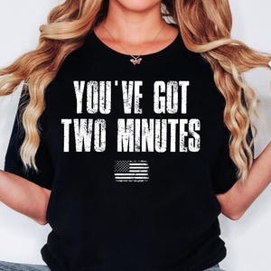 Könnte beinhalten: Schwarzes T-Shirt mit weißem Text "You've got two minutes" und einer Grafik einer abgenutzten amerikanischen Flagge.
