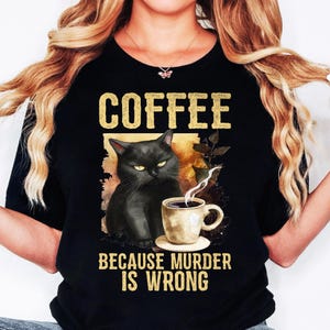 Peut inclure: T-shirt noir avec un chat noir tenant une tasse de café. Le texte sur le t-shirt est "Coffee because murder is wrong."