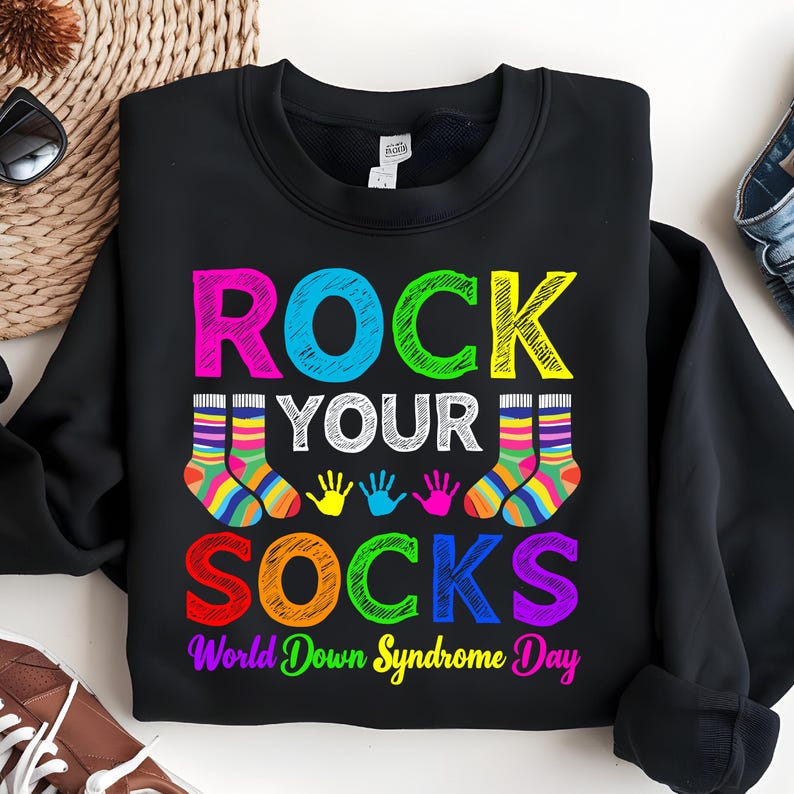 May include: Black sweatshirt with the text "Rock Your Socks" in colorful letters. The text is surrounded by colorful handprints and socks. The bottom of the sweatshirt says "World Down Syndrome Day".