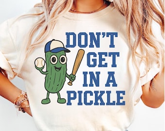 May include: Cream-colored t-shirt with a cartoon pickle character wearing a baseball cap and holding a baseball and bat. The text "DON'T GET IN A PICKLE" is printed in blue block letters.