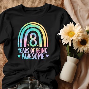 Könnte beinhalten: Schwarzes T-Shirt mit einem bunten Regenbogen-Design und der Zahl 8. Der Text lautet "8 YEARS OF BEING AWESOME" mit Herz-Akzenten. Rechts vom T-Shirt steht eine Vase mit Blumen.