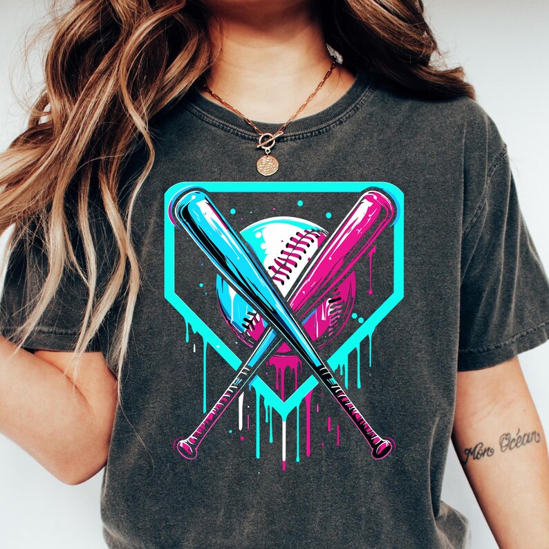 May include: A dark gray t-shirt with a graphic of a baseball diamond, two crossed bats, and a baseball. The bats are blue and pink, and the baseball is white with black stitching. The graphic has a dripping paint effect in blue and pink.