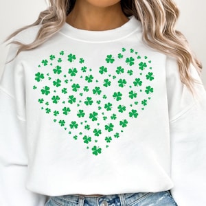 Op de afbeelding: Witte trui met een groen klavertjevier-hartontwerp. De klavertjesvier zijn in de vorm van een hart op de voorkant van de trui gerangschikt.
