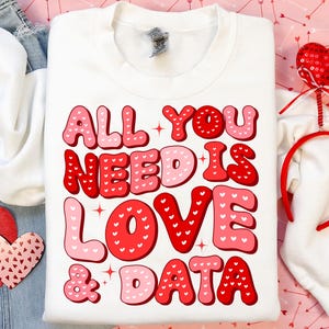 May include: White sweatshirt with a red and pink graphic that says "All you need is love & data". The letters are filled with small white hearts.