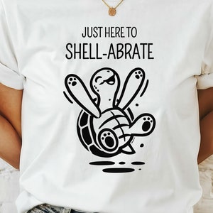 May include: White t-shirt with a black and white illustration of a turtle with the text "Just here to shell-abrate".