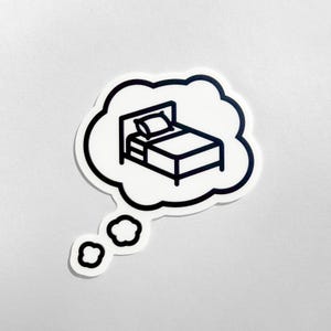 May include: A black and white sticker featuring a bed inside a thought bubble. The bed has a pillow and a nightstand. The thought bubble has a black outline and a white interior. Two smaller thought bubbles are below the main one.