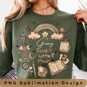 Puede incluir: Sudadera verde oliva con un diseño gráfico colorido. El diseño incluye un arcoíris, estrellas, manzanas, libros y las palabras "Growing Bright Little Minds". La frase "PNG Sublimation Design" está en la parte inferior.