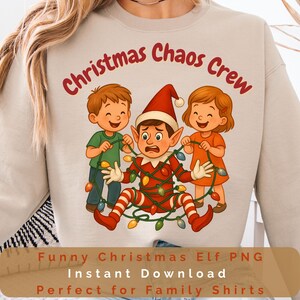 Puede incluir: Sudadera beige con un gráfico navideño. El diseño muestra un elfo enredado en luces navideñas, con dos niños sosteniendo la cadena de luces. El texto superior dice "Christmas Chaos Crew".