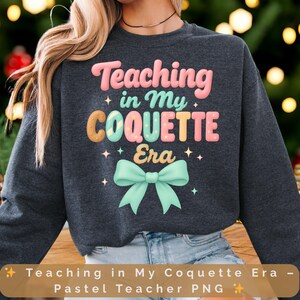 Puede incluir: Sudadera gris oscuro con el texto "Teaching in My Coquette Era" en colores pastel. El diseño incluye un lazo y estrellas. Una camiseta gráfica con temática de profesor.