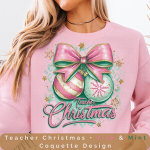 Puede incluir: Sudadera rosa con un diseño de adorno navideño. El diseño presenta un gran lazo rosa, dos adornos y las palabras "Teacher Christmas" en escritura verde. Los adornos son rosas y verde menta con detalles dorados.