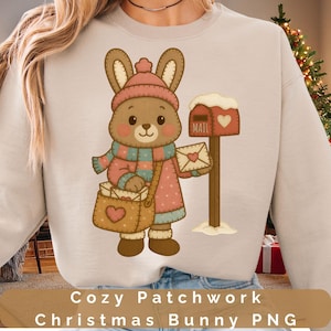 Puede incluir: Una sudadera beige con una ilustración de un conejito de dibujos animados. El conejito está vestido con ropa de invierno, sosteniendo una bolsa de correo y un sobre. Lleva un gorro, bufanda y abrigo rosas. Un buzón rojo con un corazón está a la derecha. El texto en la parte inferior dice "Cozy Patchwork Christmas Bunny PNG."