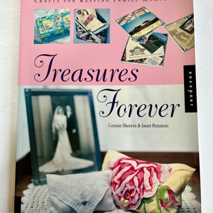 May include: A hardcover book titled "Treasures Forever" by Connie Sheerin & Janet Pensiero. The cover features a pink background with the title in elegant script, and images of keepsakes. A framed wedding photo and a floral-printed pillow are also visible.