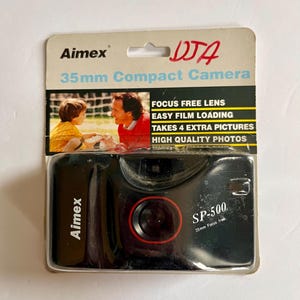 May include: A black Aimex SP-500 35mm compact camera in its original packaging. The packaging features the Aimex logo, camera specifications, and a photo of a man and child. The camera has a red lens.