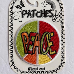 May include: A circular iron-on patch featuring a peace sign design divided into four colored segments of lime green, red, orange, and yellow. The word PEACE is embroidered in bold, multi-colored letters across the center of the patch.