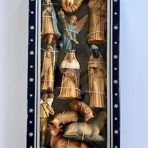 May include: A boxed nativity set featuring molded plastic figurines including a central infant, an angel, three kings, a shepherd, and various animals. The dark blue rectangular box is decorated with white star patterns and contains the figures.