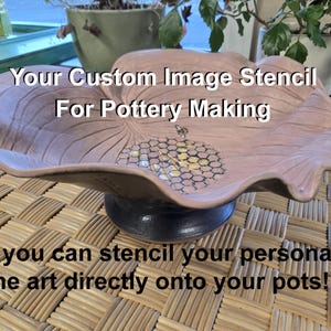 May include: A pink ceramic bowl with a honeycomb design and a bee. The bowl is on a woven mat. The text "Your Custom Image Stencil For Pottery Making" is above the bowl. The text "Now you can stencil your personalized line art directly onto your pots!" is below the bowl.