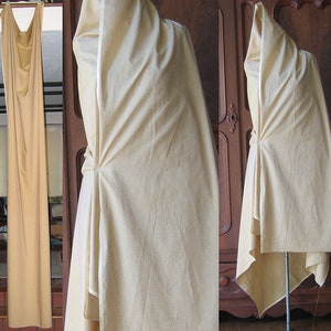 Könnte beinhalten: Ein beigefarbener Stoff, der über eine Kleiderpuppe drapiert ist und die Konstruktion eines Kleides mit hohem Ausschnitt und einem langen, fließenden Rock zeigt.