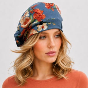 May include: A blue beret featuring a vibrant floral pattern with orange, red, and white flowers. The hat has a wide, solid blue band at the base and a rounded, soft crown that sits comfortably on the head, showcasing a detailed botanical print.