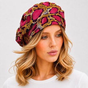 May include: A slouchy beret-style hat featuring a vibrant snake skin pattern in shades of magenta, mustard yellow, and black. The fabric has a subtle sheen and a gathered, rounded silhouette that sits comfortably on the head with a soft, draped fit.