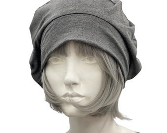 May include: A gray, slouchy beanie hat made of soft fabric. The hat is displayed on a mannequin head with short, gray hair. The beanie has a gathered crown and a wide, folded brim, offering a casual and comfortable style.