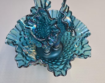 May include: A vintage, iridescent blue glass bowl with a ruffled edge and a decorative handle. The bowl has a textured surface with a pattern of small bumps. The handle is a stylized, curved design.
