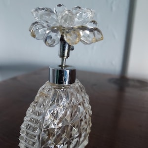 May include: A clear glass perfume bottle with a faceted design and a crystal flower stopper.