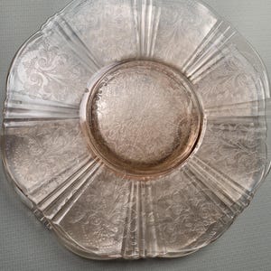 May include: A stack of clear glass plates with a floral etched design. The plates have a scalloped edge and a raised center. The plates are likely vintage and suitable for serving food.