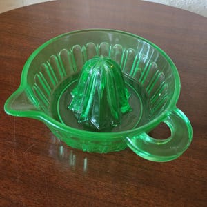 Peut inclure: Presse-agrumes vintage en verre vert avec bec verseur et poignée. Le presse-agrumes présente un bol côtelé et un presse-agrumes central pour extraire le jus. La couleur vert vif et le design classique suggèrent un outil de cuisine.
