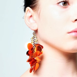 May include: Orange and gold sequined dangle earrings with a brown beaded chain.