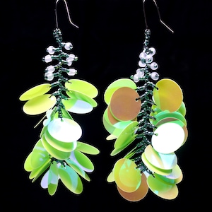 May include: A pair of long, dangling earrings with green beads and iridescent green and white sequins. The earrings are made with a beaded chain and have a teardrop shape.