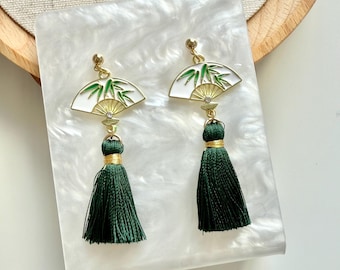 May include: A pair of green tassel earrings with a white and gold fan-shaped charm featuring a bamboo design.