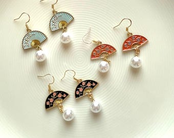 May include: Three pairs of gold earrings with a pearl dangle. Each earring features a fan-shaped charm with a floral design. The fans are blue, red, and black.