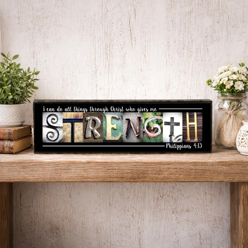 May include: A black wooden sign with the word "STRENGTH" spelled out in various textures and colors. The sign includes the text "I can do all things through Christ who gives me - Philippians 4:13."