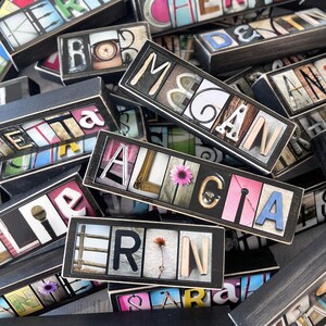 May include: A collection of personalized wooden name blocks. Each block features a name spelled out with individual letter tiles, set against various background images and colors. Some blocks include decorative elements like flowers.