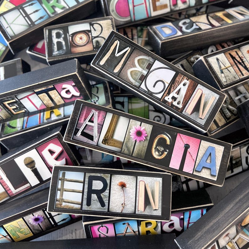 May include: A collection of personalized wooden name blocks. Each block features a name spelled out with individual letter tiles, set against various background images and colors. Some blocks include decorative elements like flowers.