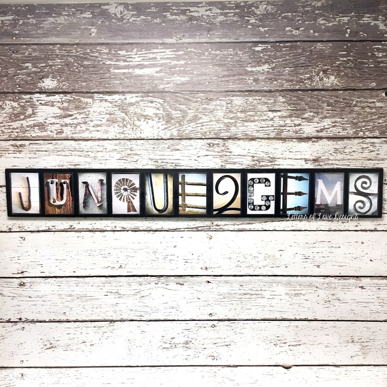 Puede incluir: Una pieza de arte mural enmarcada que deletrea "JUNE GEMS" en baldosas de letras individuales. Cada letra presenta un dise&ntilde;o &uacute;nico, que incluye un molino de viento, una valla y elementos decorativos. El fondo es una pared de madera blanca y gris desgastada.