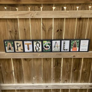Puede incluir: Un letrero rectangular con la palabra "ARTSGALA" deletreada en bloques de letras individuales. Cada bloque de letras presenta una imagen o dise&ntilde;o diferente. El letrero tambi&eacute;n incluye el texto "WRIGHT STATE UNIVERSITY COLLEGE OF LIBERAL ARTS".