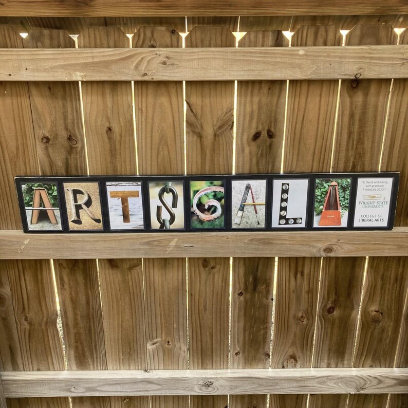 Puede incluir: Un letrero rectangular con la palabra "ARTSGALA" deletreada en bloques de letras individuales. Cada bloque de letras presenta una imagen o dise&ntilde;o diferente. El letrero tambi&eacute;n incluye el texto "WRIGHT STATE UNIVERSITY COLLEGE OF LIBERAL ARTS".